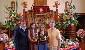 Olivia Black (6) and Sophie Black (5) add their own floral contribution to the beautiful Harvest decorations at Ballinderry Moravian Church last Sunday morning, which included corn arranged in a crisscross display around the front of the pulpit. Included in the picture are Sr Patsy Holdsworth (left) and Sr Violet Best (right).
