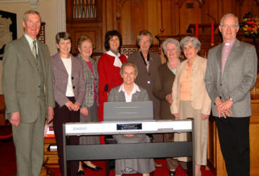 Pictured at the dedication of a new digital piano is L to R: Ivor Ferguson, Elizabeth Bridgett, Phyllis Spence, Janet Ferguson (Director of Music), Edith McConnell, Norma Coggins, Anthea Harrison, the Rev Brian Gibson and organist Dr Bertha Cowan (seated at the piano.)