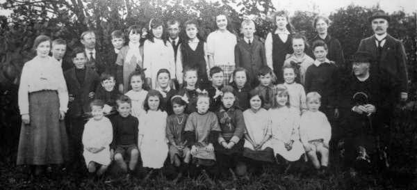 Year 1920 approx: L to R: (back row) Miss Kate Gilmore (Teacher), Alex Kerr, John Wilson, William Wylie, Eric Foster, Sarah Cochrane, Susan Dickinson, Hugh/Jim Ruddock, Georgina McConnell, Susan McClinton, Thomas Kerr, Lottie McConnell, Charlotte Sayers,