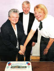 Canon Ken McReynolds looks on as Pat Harvey and Sister Myrtle Morrison cut the 1Oth anniversary cake.