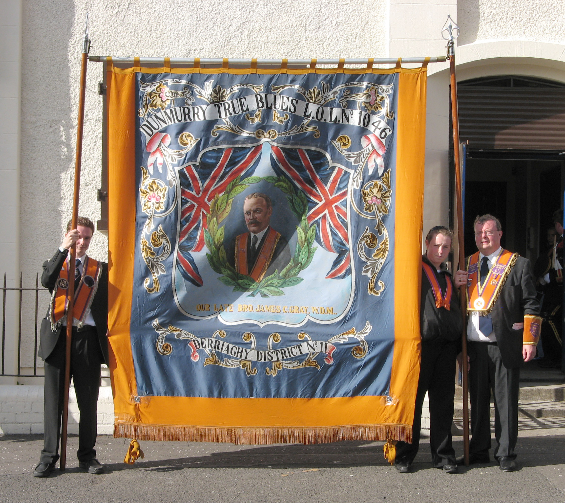 Bro James Connor Gray (Worshipful District Master of Derriaghy LOL No 11) pictured with his daughter Hannah (right) and son Matthew with the banner showing a painting of his grandfather, the late Bro James Connor Gray PDM, who was present when the foundation stones of both Dunmurry Orange Hall and Saint Colman�s Parish Church in 1908 were laid.