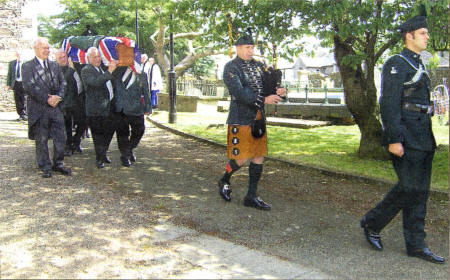 A piper leads Mr Moore's coffin to the church for the funeral service .