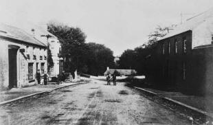 Glenavy Main Street before the erection of the First World War memorial. The school is in the background, behind the man with the horse. William McKeown's shop is to the left, where the men are standing. The shop building still remains, though the fine houses beside it have been demolished. The right side of the street is basically unchanged. (Photograph courtesy of Brian McKeown, Belfast.) 